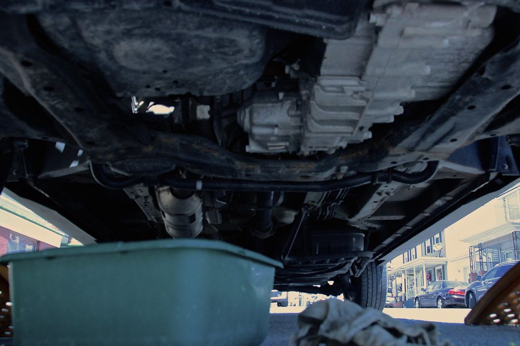 Underside of a raised car with a drain pan positioned under the engine oil pan