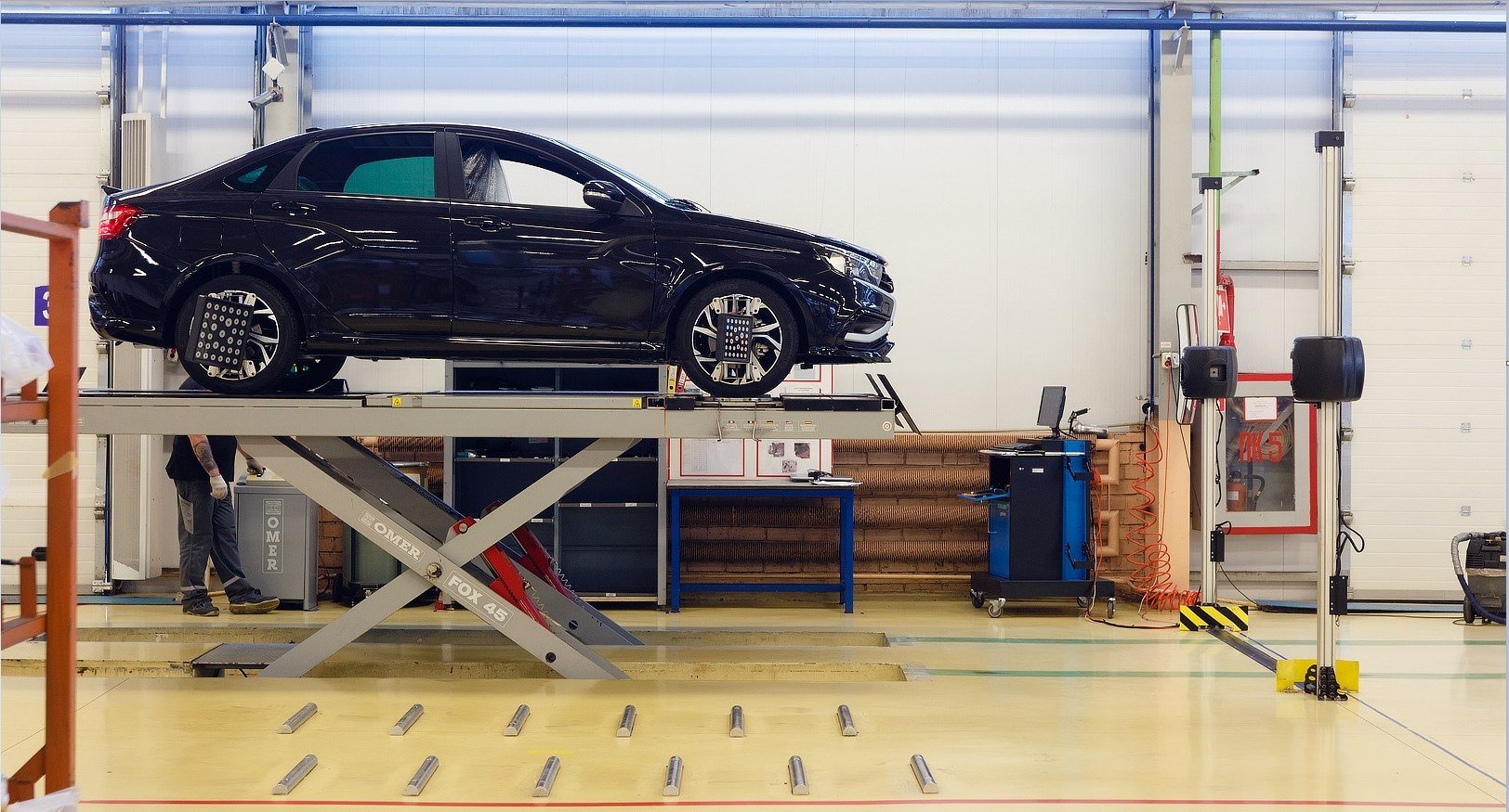 Car raised on an alignment rack with a wheel alignment machine and camera tower in a service bay